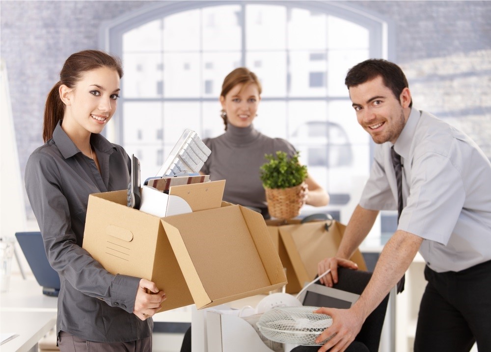 3 people in business attire holding moving boxes