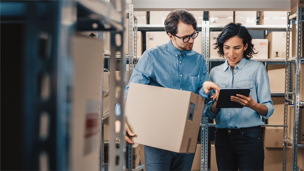 two people looking at a tablet in a warehouse full of boxes