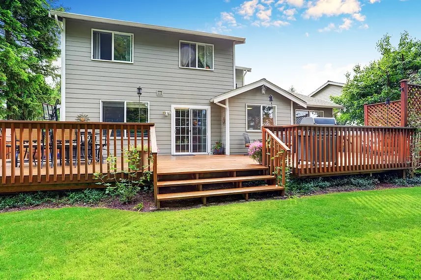 A two-story house with a wooden deck with railings, steps leading to a green lawn