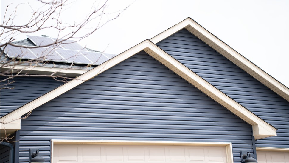 close up of blue home garage, behind the garage are solar panels installed on the roof.