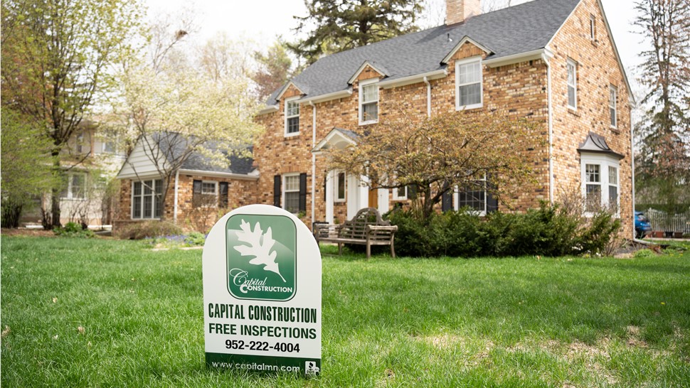 white yard sign stuck in grass in front of brick house, the sign reads Capital Construction in green writing