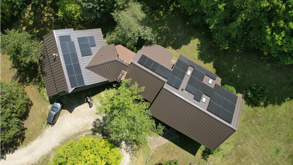 drone image of brown metal roof and solar panels in the middle of the forrest