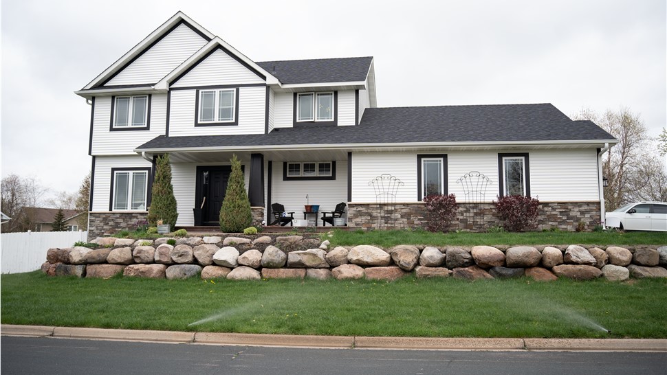 White two story home with black trim around the windows and sides, and boulder retaining wall in the front yard
