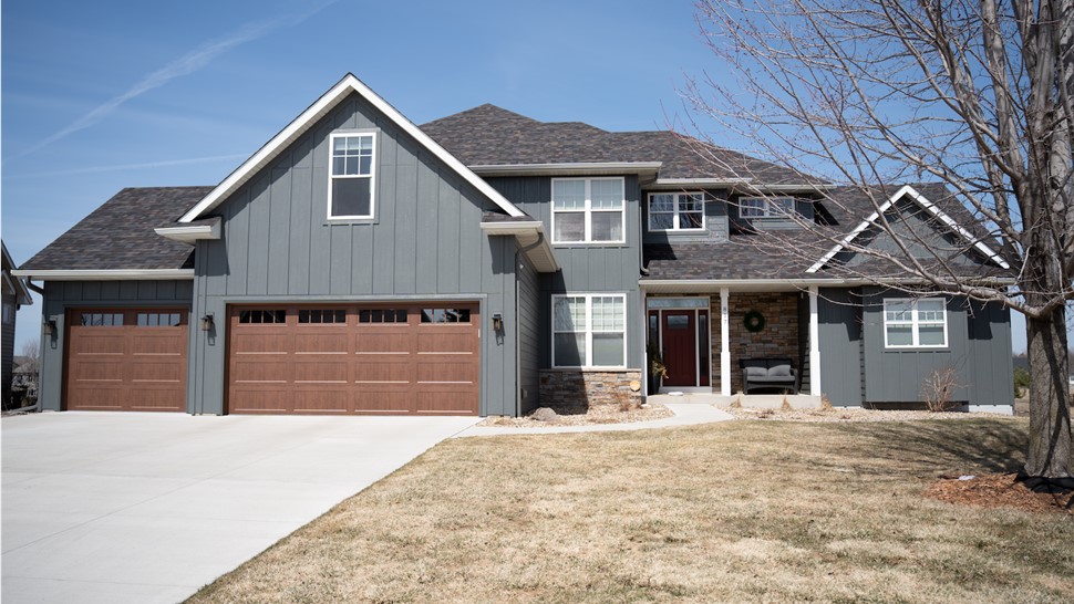 Dark gray two story home with red front door, stone work, and large garage on sunny day
