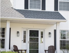 close up of white home front door, two wood outdoor chairs sit on the front porch, one on either side of the front door
