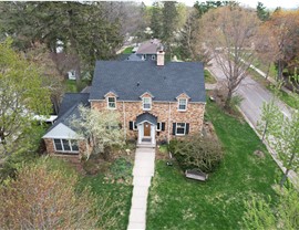 Drone image taken of brick two story home and dark gray shutters, it is an angle so you can see the front of the home