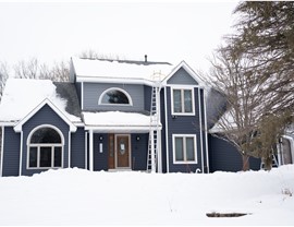 royal estate vinyl siding, two story blue and gray home. there is a ladder to the top of the roof, where there is lots of snow