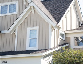 close up of yellow tan board and batten siding and dark gray roof shingles