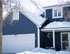 close up of a two story navy blue home with white posts and white siding  and white garage door