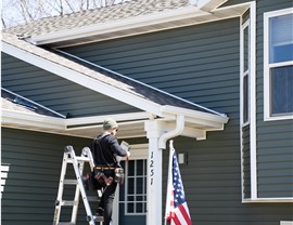 Man standing on ladder installing white gutters  in front of the front door