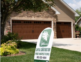 white and green yard sign in front of brown home with brown garage doors