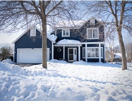 two story navy blue home with white garage door and two bare trees in the snowy front yard