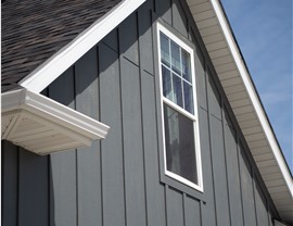 The highest elevation of of a home which is sided with gray board and batten. In the triangle the elevation makes sits a window with white trim.