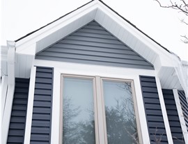 Close up of royal estate siding in marine blue and storm. there is a window in the elevation and the top of the elevations is gray. Around the window is blue siding