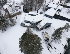 Blue and gray two story home taken from a drone. The roof is white, covered in snow. There is a construction van parked in the driveway.