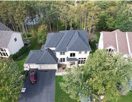 drone image of tan stucco two story home with black roof