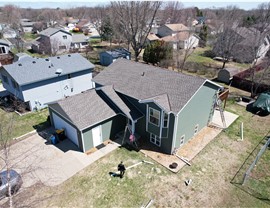 drone image of home, man is walking through the front yard towards the front door, the home is green and has a brown roof