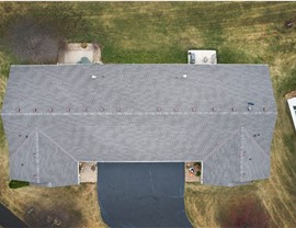 Picture of a townhome taken directly above, the roof is a gray color and the townhome has one dark black driveway leading up to it.