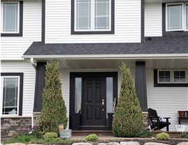 modern farmhouse in souther minnesota, close up of black front door. white house with black trim. Bordering the front door are two groomed pine trees