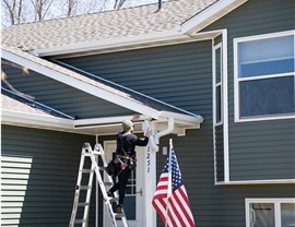 man on ladder installing white gutters on one story green home