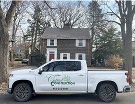 white truck marked in front of a cape cod style home, the truck has a green logo that reads capital construction