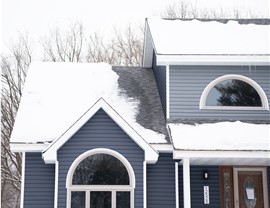 left side of a two story blue and gray home. The home has a brown front door and lots of snow on the roof