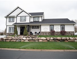 White two story home with black trim around the windows and sides, and boulder retaining wall in the front yard