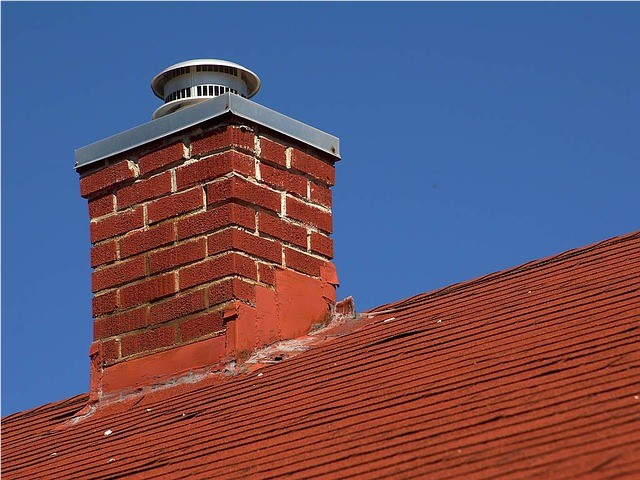 A red brick chimney with a metal chimney crown and a galvanized chimney cap. 
