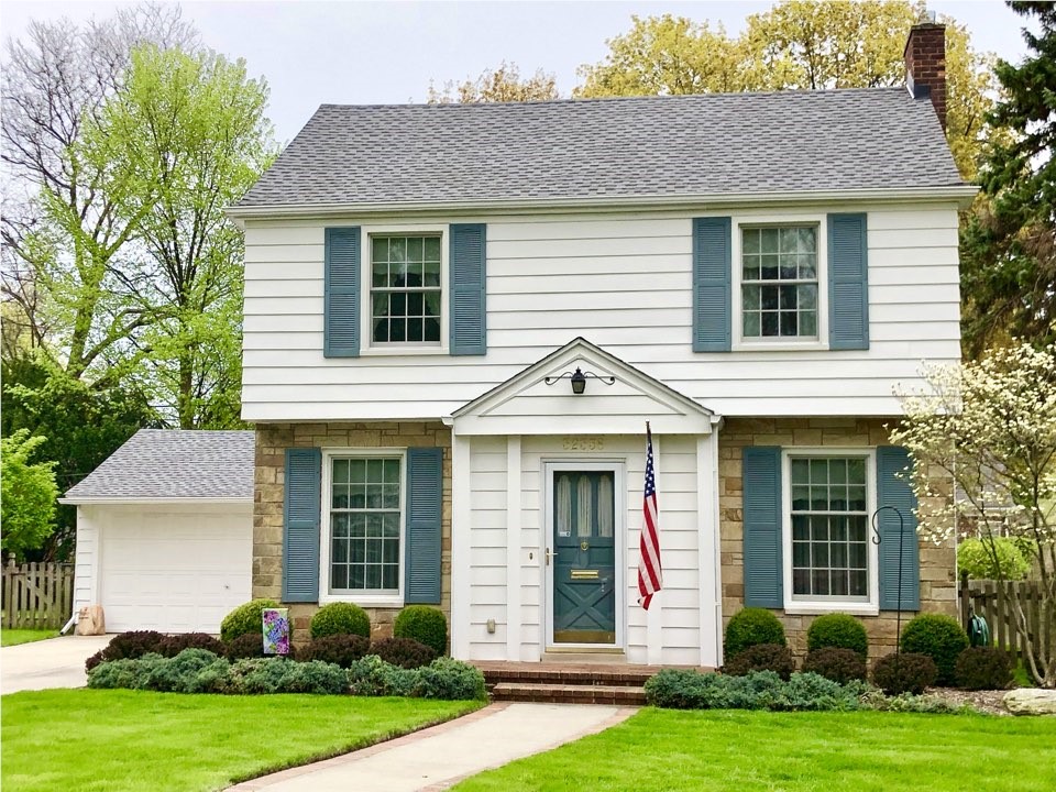 A white two-story home with a blue shutters that has recently had a new shingled roof installed.