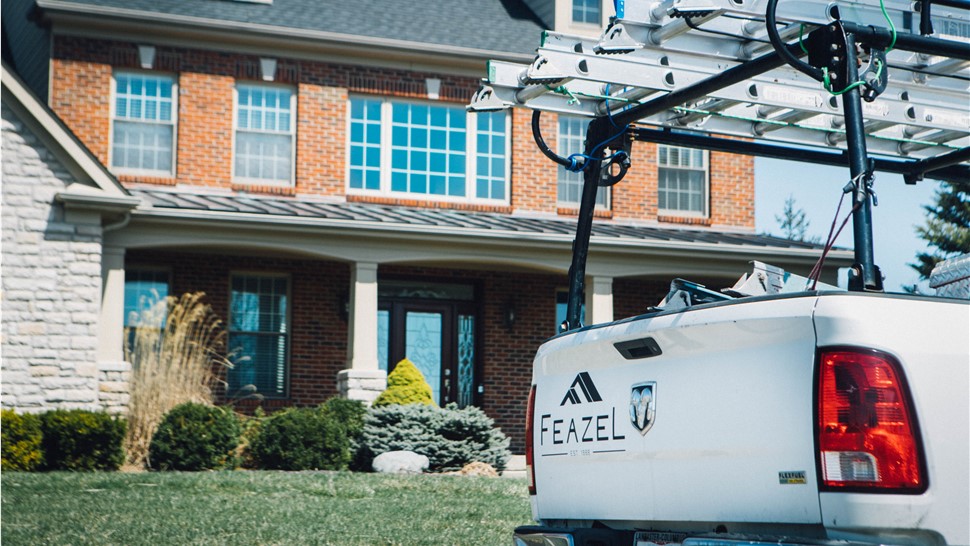The back of a pickup truck with a Feazel logo is parked in front of a brick home