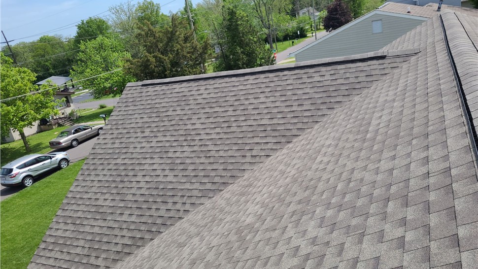 Close-up view of a Weathered Wood Timberline HDZ shingle roof replacement in Blue Ash, highlighting the textured pattern and professional installation in a residential neighborhood with trees and parked cars visible in the background.