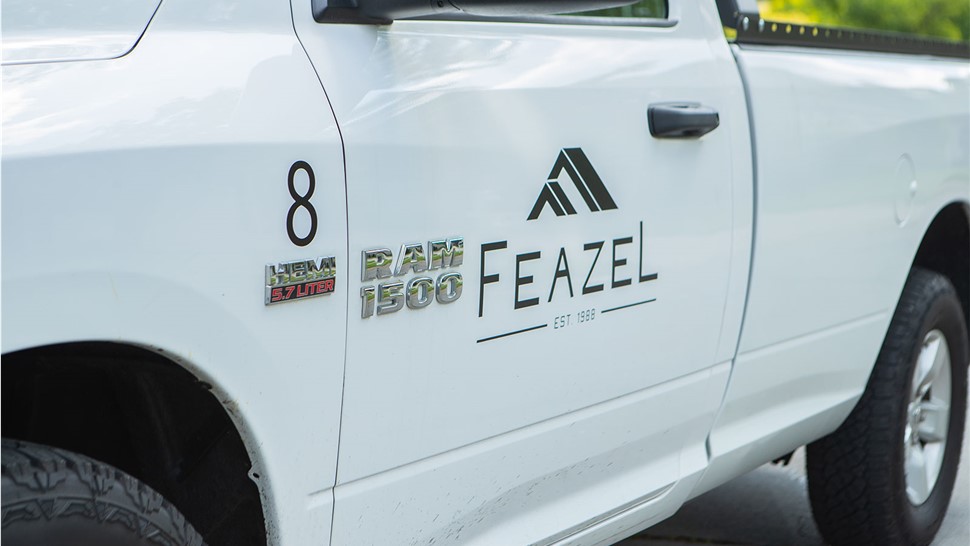 The side of a white pickup truck with the word Feazel on the door