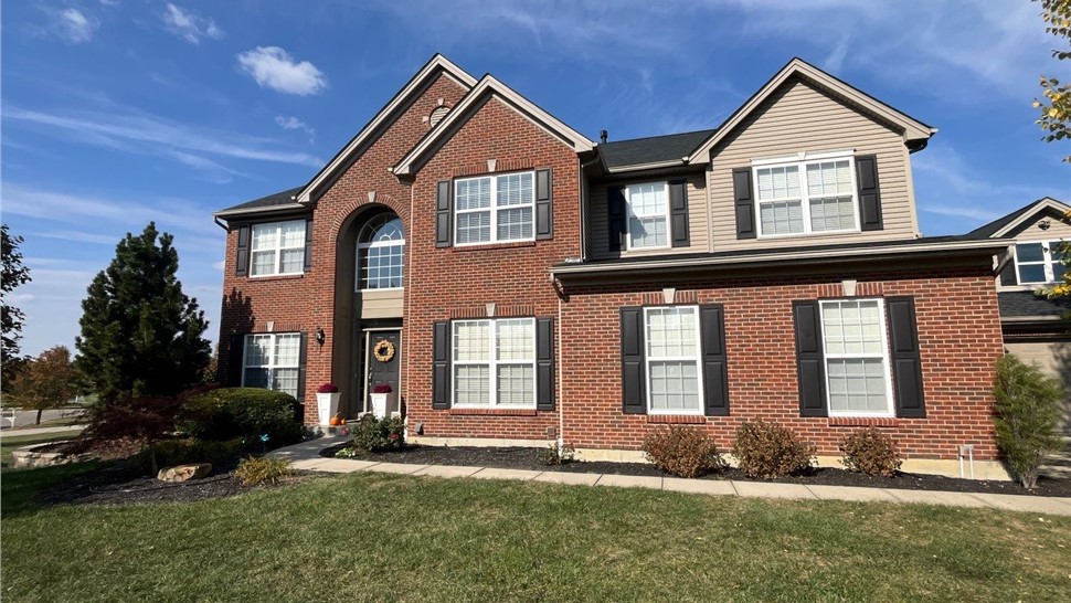 Middletown, Ohio home with a newly installed roof featuring Charcoal Timberline HDZ shingles, beautifully paired with a red brick facade and a clear blue sky in the background.