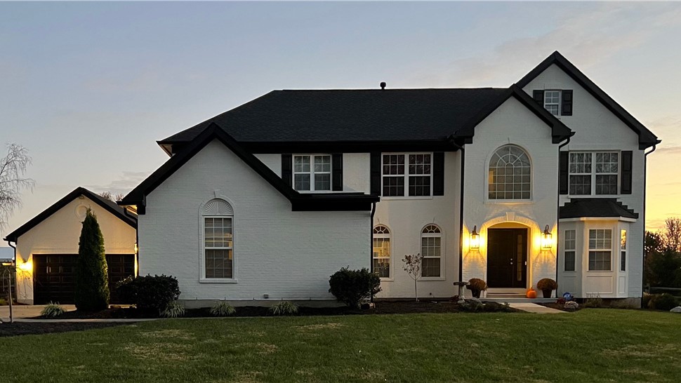 A two-story white brick home in Maineville, Ohio, with a newly installed Charcoal Timberline HDZ shingle roof, black trim, and exterior lighting at sunset. The home features a well-maintained lawn and landscaping.
