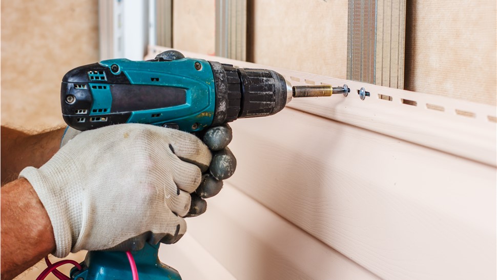 A man screws a new panel of siding on the side of a house