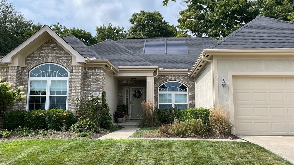 Front view of a Newark, OH home featuring a new Williamsburg Slate Timberline HDZ roof with integrated solar panels. The home has a brick and stucco exterior, arched windows, and well-maintained landscaping with a lush green lawn.