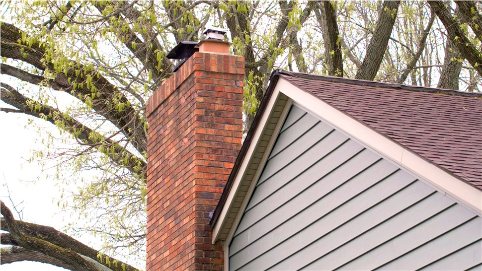 A red brick chimney on a home with vinyl siding