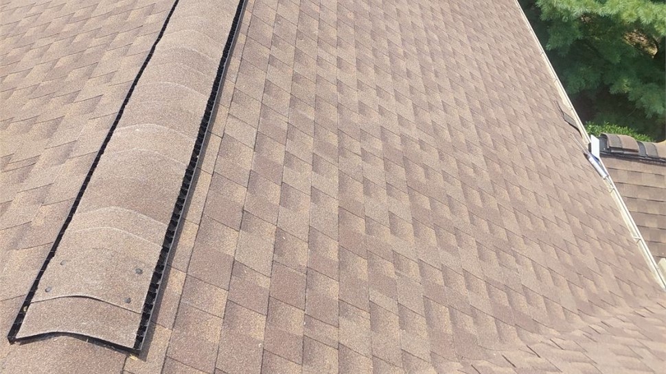Close-up of a roof in Fairfield, Ohio, with Barkwood Timberline HDZ shingles, showcasing a ridge vent system and earthy brown tones, surrounded by green trees and neighboring houses.