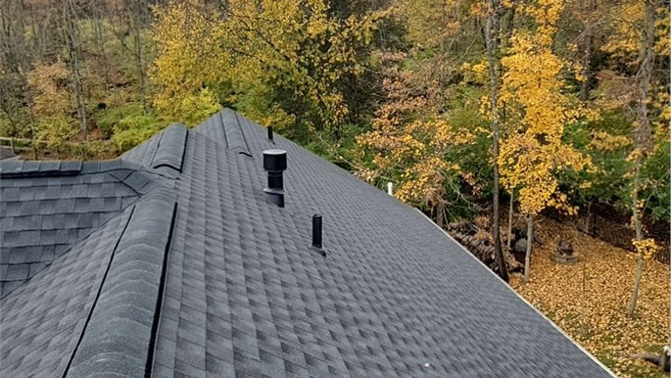 Newly installed Charcoal Timberline HDZ shingle roof in Goshen, Ohio, with ridge cap and vent pipes visible, set against a scenic autumn backdrop with trees showcasing vibrant fall colors.