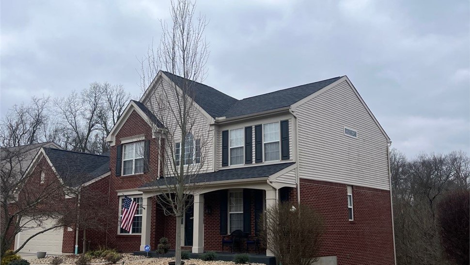 Two-story brick and vinyl-sided home in Cleves, OH, with a new roof featuring Charcoal Timberline HDZ shingles from GAF, complemented by a covered front porch and landscaped yard.