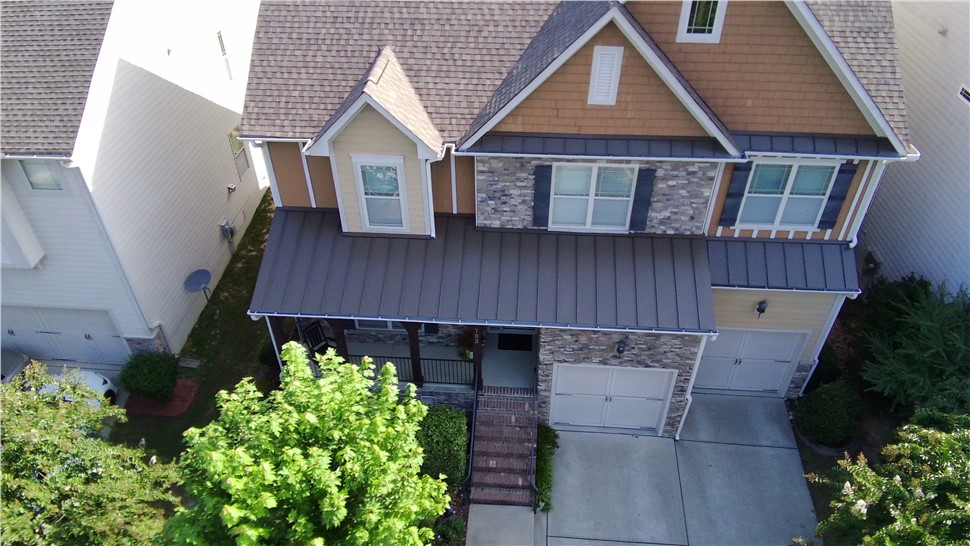 Aerial view of a Cary, NC home with a new Golden Harvest Timberline HDZ shingle roof, featuring dormer windows, a metal porch roof, stone and siding exterior, and a two-car garage.