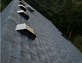 Close-up view of a new roof installation in Blue Ash, OH, featuring Pewter Gray Timberline HDZ shingles with multiple attic vents for proper ventilation, surrounded by trees in the background.