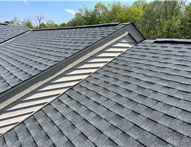 A newly installed Pewter Gray Timberline HDZ shingle roof in Milford, OH, featuring precise alignment and light-colored siding. The backdrop includes green trees and a clear blue sky.