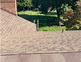 New roof in Fairfield, Ohio, with Weathered Wood Timberline HDZ shingles, a brick chimney, ridge vent system, and a backdrop of green trees and a manicured lawn.