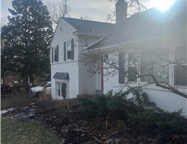 White brick home in Hyde Park, OH, with a newly installed Charcoal Timberline HDZ shingle roof, black shutters, and a black metal awning, surrounded by a winter landscape with light snow on the ground.