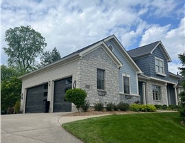 Modern two-story home in Cleves, OH, showcasing a new roof with Pewter Gray Timberline HDZ shingles, stone and siding exterior, dark garage doors, and neatly landscaped yard with shrubs and mulch.