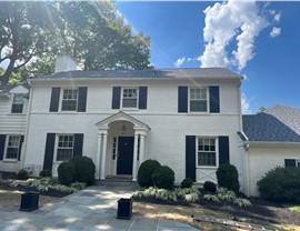 A classic white brick colonial home in Indian Hill, Ohio, featuring a newly installed Pewter Grey Timberline HDZ roof. The house has black shutters, a landscaped front yard, and a stone walkway leading to the entrance under a bright blue sky.