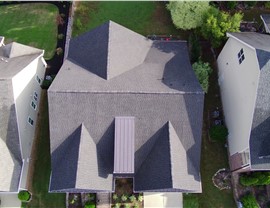 Aerial view of a Wake Forest, NC, home featuring a newly installed Appalachian Sky Timberline HDZ roof with multiple peaks and ridges, a metal accent roof, and a landscaped backyard, situated between two neighboring houses.