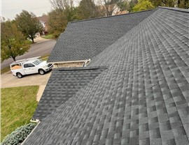 Close-up view of a newly installed Charcoal Timberline HDZ shingle roof in Hamilton, OH. The dark gray shingles are neatly arranged, with a white Feazel work truck visible in the driveway and a suburban neighborhood in the background.