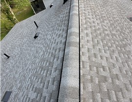 New Pewter Gray Timberline HDZ shingle roof in Goshen, Ohio, featuring a ridge vent for ventilation. A roofer’s boots are visible, showing the final inspection or completion of the project, with houses and trees in the background.
